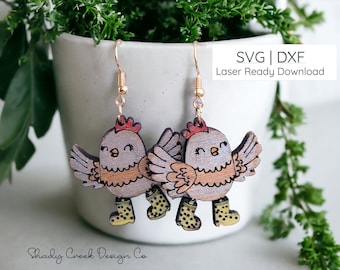 May include: A pair of wooden earrings featuring a cartoon chicken design. The chickens are wearing yellow rain boots and have a light brown and gray color scheme. The earrings are laser cut and ready to download as SVG and DXF files.