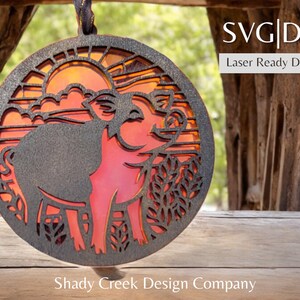 Puede incluir: Un adorno de madera cortado con láser que presenta la silueta de dos cerdos en una escena de puesta de sol. El adorno está pintado en tonos de naranja, rojo y negro. El texto "SVG|DXF Laser Ready Download" es visible en la esquina superior derecha de la imagen.
