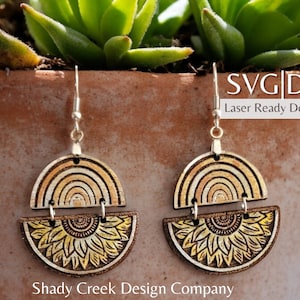May include: A pair of laser cut wooden earrings featuring a sunflower design with a rainbow arch above it. The earrings are gold and brown in color. SVG | DXF Laser Ready Download.