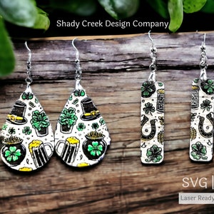 May include: Two pairs of laser cut earrings with a St. Patrick's Day theme. One pair is teardrop shaped with a white background and green shamrocks, gold coins, beer mugs, and leprechaun hats. The other pair is rectangular with a white background and green shamrocks, gold horseshoes, and beer mugs.