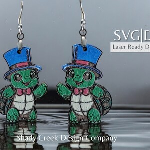 May include: A pair of laser cut wooden earrings featuring a cartoon turtle wearing a blue top hat and bow tie. The earrings are designed for crafting and are available as SVG and DXF files.
