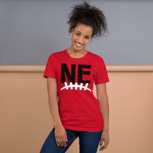 Op de afbeelding: Rood T-shirt met korte mouwen met een zwart-witte afbeelding van de letters "NE" met een voetbalnaadontwerp eronder.