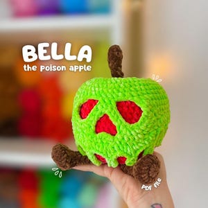 May include: A crochet plush toy shaped like a green apple with a skull-like face featuring red cutouts. The apple has a brown stem and small brown feet. Text on the image reads BELLA the poison apple and PDF file.