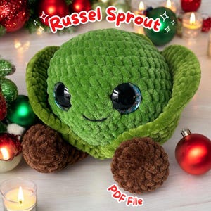Könnte beinhalten: Ein grünes Plüsch-Brüsseler-Sprout-Spielzeug mit großen, glitzernden Augen und einem lächelnden Gesicht. Das Spielzeug hat braune, strukturierte Füße und ist von Weihnachtsdekorationen und Kerzen umgeben. Der Text "Russel Sprout" wird über dem Spielzeug angezeigt.