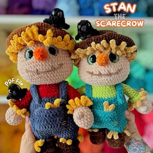 May include: Two handmade crochet scarecrow dolls, each with a straw hat, orange nose, and smiling face. One wears blue dungarees over a red shirt, the other wears blue dungarees over a green shirt. Each has a black crow on its hat. Text reads "STAN THE SCARECROW".