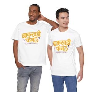 Könnte beinhalten: Zwei weiße T-Shirts mit dem orangefarbenen Text "बाकरवडी फॅन" mit dekorativen Elementen und dem Satz "BAKARWADI FOREVER". Die T-Shirts werden von zwei Personen getragen. Der Text ist in einer Schriftart geschrieben.