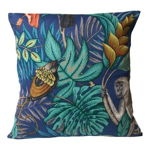 May include: Square cushion with a tropical jungle design. The cushion has a dark blue background with a pattern of large green leaves, orange flowers, and a bird with yellow and brown feathers. A monkey is also visible.