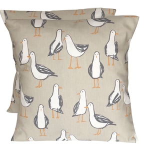May include: Two beige pillow covers featuring a repeating pattern of white seagulls with black markings and orange beaks.