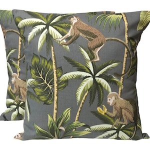 May include: Two grey throw pillows with a tropical print featuring monkeys and palm trees. The pillows have a green, brown and white design.