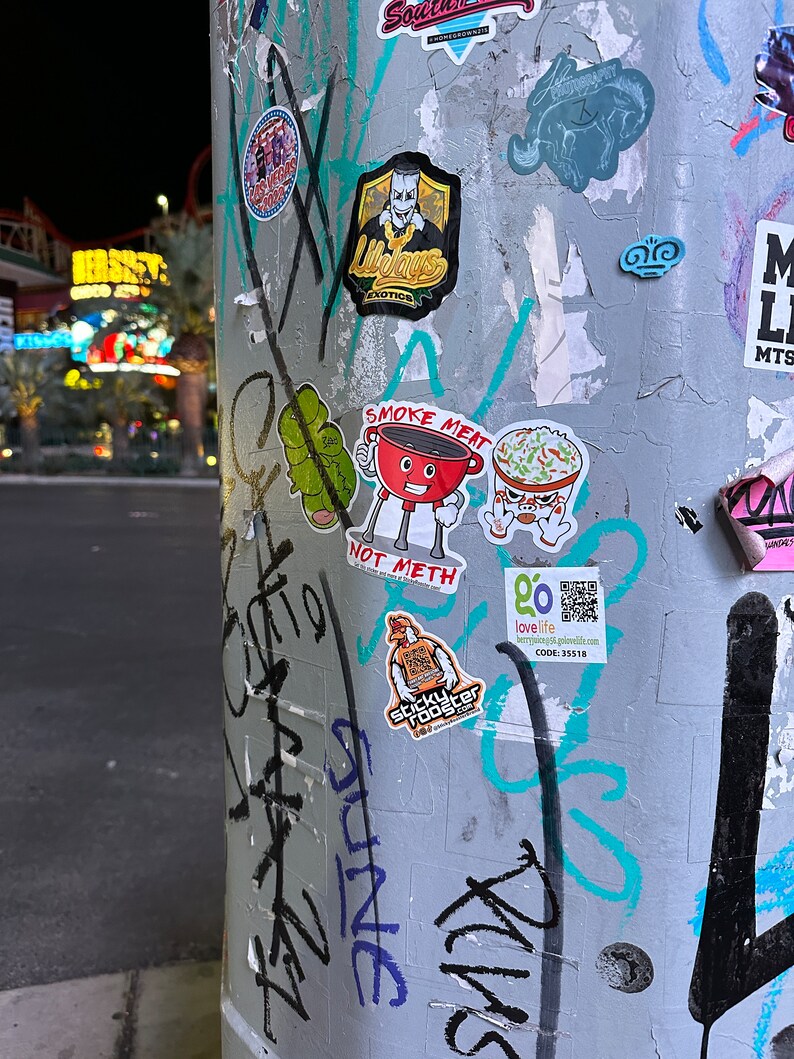 Smoke Meat Not Meth sticker with a little grill giving a thumbs up. Sticker is on a pole with other stickers.