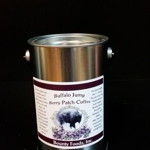 Könnte beinhalten: Ein silberner Metallbehälter mit einem schwarz-weißen Etikett. Das Etikett trägt die Aufschrift "Buffalo Jump Berry Patch Coffee" und zeigt eine Schwarzweißillustration eines Büffels. Das Etikett enthält auch den Firmennamen "Bounty Foods, Inc."