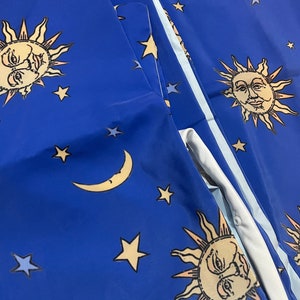 May include: Blue fabric with a repeating pattern of suns and stars. The suns have faces and are surrounded by rays. The stars are yellow and blue.