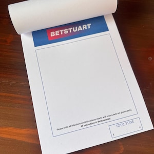 May include: A white betting slip with a blue and red header that says "BETSTUART". The slip has a blank space for writing bets and a section at the bottom labeled "TOTAL STAKE" with spaces for pounds and pence.