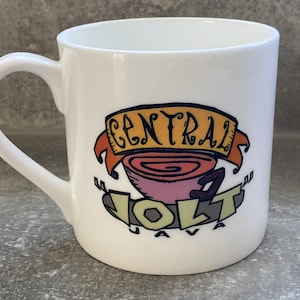May include: White ceramic coffee mug with a curved handle. The mug features a colourful graphic with the words "CENTRAL JAVA JOLT" in a stylised design, including a coffee cup illustration.