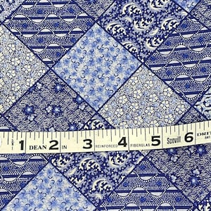 May include: Close-up of a blue and white patterned fabric with a patchwork design. A measuring tape shows 6 inches. The fabric features various floral and geometric patterns in shades of blue and white.