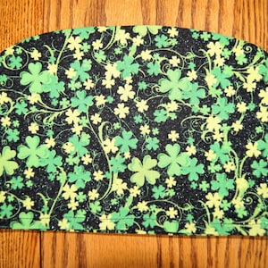 May include: A black fabric tea cozy with a green shamrock and swirl pattern. The fabric has a glittery finish.