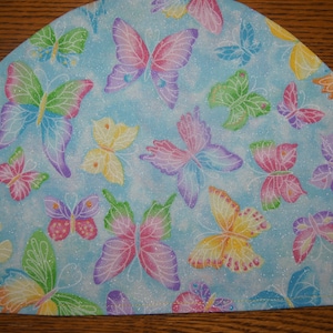 May include: A light blue fabric with a repeating pattern of colorful butterflies. The fabric has a glittery finish.