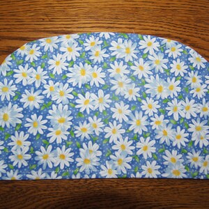 May include: A blue fabric pot holder with a white daisy pattern. The pot holder is shaped like a half-circle.