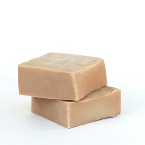 May include: Two bars of beige soap stacked on top of each other. The soap is rectangular and has a smooth surface.