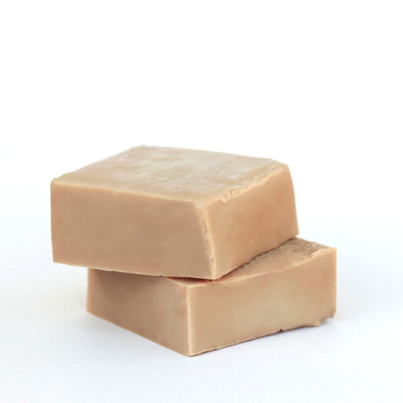 May include: Two bars of beige soap stacked on top of each other. The soap is rectangular and has a smooth surface.