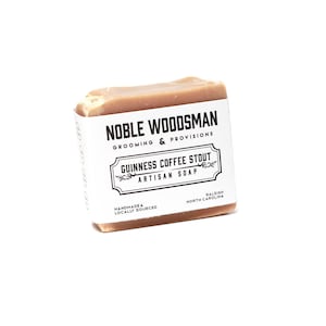 May include: A bar of brown soap with a white label that reads "NOBLE WOODSMAN GROOMING & PROVISIONS GUINNESS COFFEE STOUT ARTISAN SOAP HANDMADE & LOCALLY SOURCED RALEIGH NORTH CAROLINA"