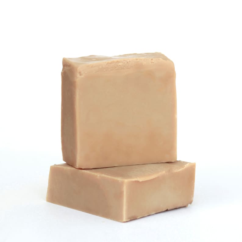 May include: Two bars of beige soap stacked on top of each other. The soap is rectangular and has a smooth surface.