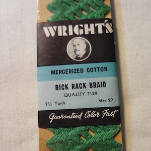 Puede incluir: Un paquete de galón de algodón mercerizado verde, etiquetado con "WRIGHTS" y el texto "MERCERIZED COTTON", "RICK RACK BRAID", "QUALITY 7129", "2 1/2 Yards", "Size 29" y "Guaranteed Color Fast".