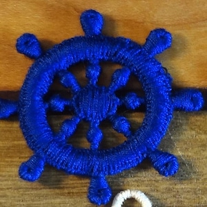 May include: Three nautical-themed decorative wheels in red, blue, and white. Each wheel has a circular design with spokes and a central hub, resembling a ship's steering wheel. The wheels are made of a textured material.