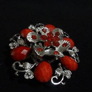 May include: A silver brooch with a red rhinestone butterfly design and red glass beads. The brooch has a floral design with intricate details.