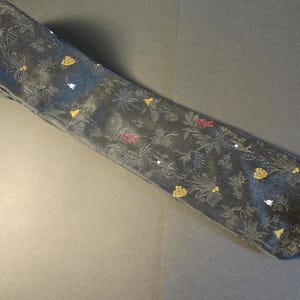 May include: A dark gray necktie with a floral pattern and gold, red, and white accents. The tie has a repeating design of flowers and leaves. The tie is made of a shiny fabric.