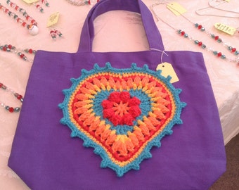 May include: Purple tote bag with a crocheted heart in shades of orange, yellow, red, and blue.