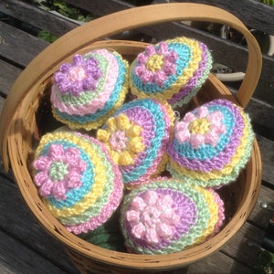 May include: A basket filled with six crocheted Easter eggs in pastel colors. The eggs are decorated with a flower pattern in pink, yellow, and blue.
