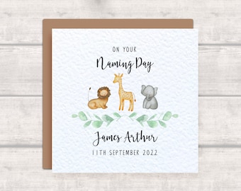 Op de afbeelding: Een witte kaart met een bruine envelop. De kaart heeft een aquarel-illustratie van een leeuw, een giraffe en een olifant met groene bladeren. De tekst op de kaart luidt "On your Naming Day, James Arthur, 11th September 2022".