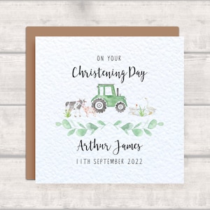 Könnte beinhalten: Ein grüner Traktor mit einer Kuh, einem Schwein und zwei Gänsen auf weißem Hintergrund mit grünen Blättern. Der Text "On your Christening Day" befindet sich über dem Traktor und der Text "Arthur James 11th September 2022" unter dem Tracteur.