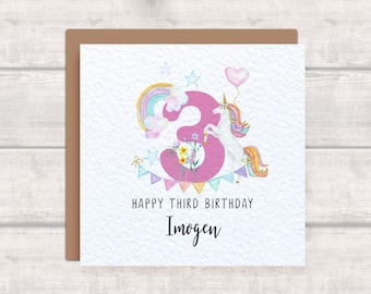 May include: A birthday card with a watercolor design. The card features a large pink number 3 with a rainbow, unicorn, and flowers. Text reads "HAPPY THIRD BIRTHDAY" and "Imogen". A heart-shaped balloon is also present.