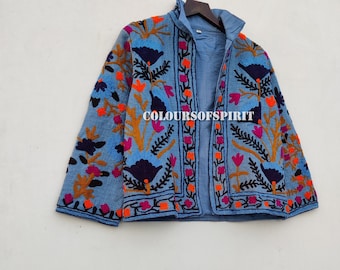 Puede incluir: Una chaqueta bordada de color azul claro con diseños florales en tonos rosa, naranja, azul y negro. La chaqueta tiene un cuello mandarín y un cierre frontal.