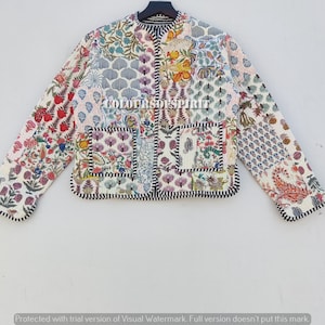 Puede incluir: Una chaqueta acolchada blanca con un diseño de patchwork que presenta patrones florales y geométricos. La chaqueta tiene un cuello alto, una cremallera y dos bolsillos de parche.