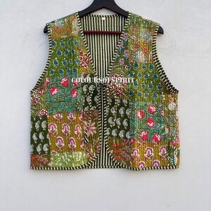 May include: A quilted vest with a patchwork design featuring floral and paisley patterns in shades of green, red, and purple. The vest has a striped interior and the text "COLOURS OF SPIRIT".