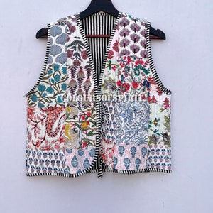 May include: A white quilted vest with a patchwork design featuring various floral patterns in shades of pink, blue, green, and yellow. The vest has a V-neck and a black and white striped lining.