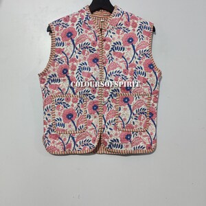 Peut inclure: Un gilet sans manches blanc avec un imprimé floral dans les tons rose et bleu. Le gilet a un col mandarin et une fermeture boutonnée. Le gilet a deux poches sur le devant.