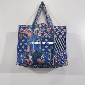 Puede incluir: Una bolsa de mano azul y blanca de patchwork con motivos florales. La bolsa tiene un borde cosido blanco y el texto "COLOURSOFSPIRIT" está impreso en la parte delantera.
