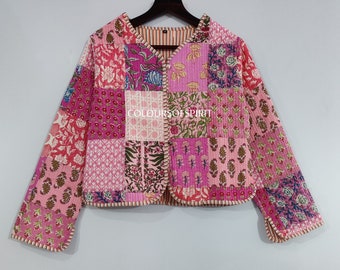 Op de afbeelding: Een roze gewatteerd jack met een patchwork-ontwerp met bloemenpatronen. Het jack heeft een V-hals en lange mouwen met een knoopsluiting. De tekst "COLOURSOFSPIRIT" is zichtbaar op de voorkant van het jack.