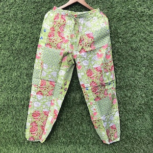 Könnte beinhalten: Hellgrüne Hose mit Patchwork-Design, bestehend aus verschiedenen Blumen- und geometrischen Mustern in Rosa-, Weiß- und Dunkelgrüntönen. Die Hose verfügt über einen elastischen Bund mit Kordelzug sowie elastische Bündchen an den Beinabschlüssen.