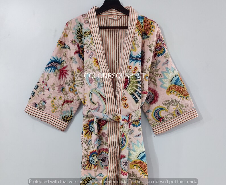 K&ouml;nnte beinhalten: Eine rosa gesteppte Robe mit Blumenmuster und gestreiftem Saum. Die Robe hat einen Bindeg&uuml;rtel und lange &Auml;rmel.