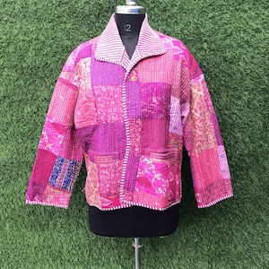 Könnte beinhalten: Eine langärmelige Steppjacke mit Patchwork-Design in verschiedenen Rosa- und Magentatönen. Das Kleidungsstück verfügt über einen Umlegekragen mit weißen und rosa Streifen, eine Knopfleiste und sichtbare Nähte auf dem gesamten Stoff.