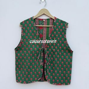 May include: A sleeveless, quilted vest in green with a repeating red floral pattern. The vest has a V-neck and a tie closure. The text "colours of spirit" is printed on the front.