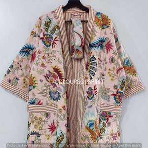 K&ouml;nnte beinhalten: Eine rosa Kimono-Robe mit floralem Druck, einer gestreiften Innenfutter und einer passenden Gesichtsmaske. Die Robe hat lange &Auml;rmel und eine Tasche auf der linken Seite. Der Text "COLOURSOF SPIRIT" ist auf die Robe gedruckt.