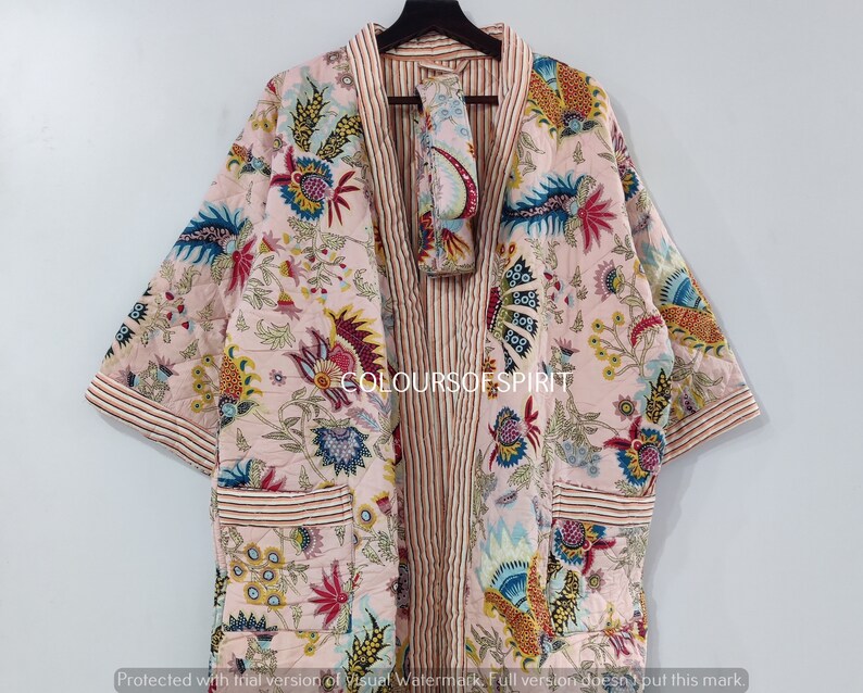 K&ouml;nnte beinhalten: Eine rosa Kimono-Robe mit floralem Druck, einer gestreiften Innenfutter und einer passenden Gesichtsmaske. Die Robe hat lange &Auml;rmel und eine Tasche auf der linken Seite. Der Text "COLOURSOF SPIRIT" ist auf die Robe gedruckt.