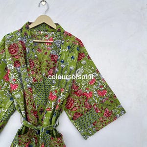 May include: A green floral print robe with a matching belt, hanging on a wooden hanger. The robe features a vibrant pattern of red, pink, blue, and white flowers and leaves. The text "colours of spirit" is visible on the robe.