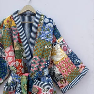 May include: A colorful patchwork robe with a striped interior and trim. The robe features a variety of floral and geometric patterns in shades of pink, blue, yellow, and green. The text "coloursofsprit" is visible on the robe.